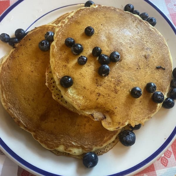 Stack of golden blueberry pancakes on a white plate with a blue rim, ready for breakfast.
