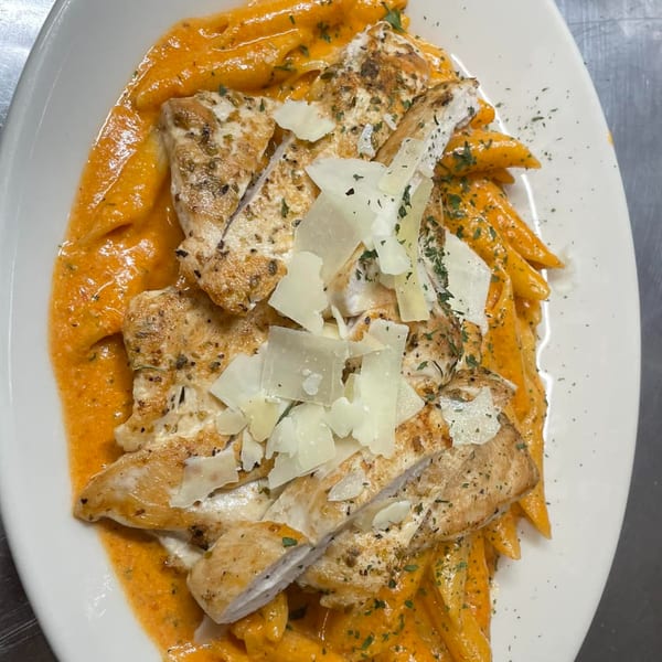 Penne pasta in creamy orange sauce topped with sliced chicken breast, parmesan, and herbs.