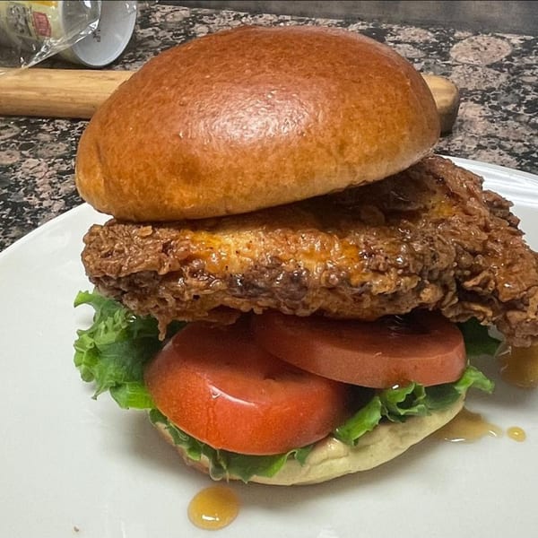 Courthouse Cafe's fried chicken sandwich with lettuce, tomato, and honey drizzle on a brioche bun.