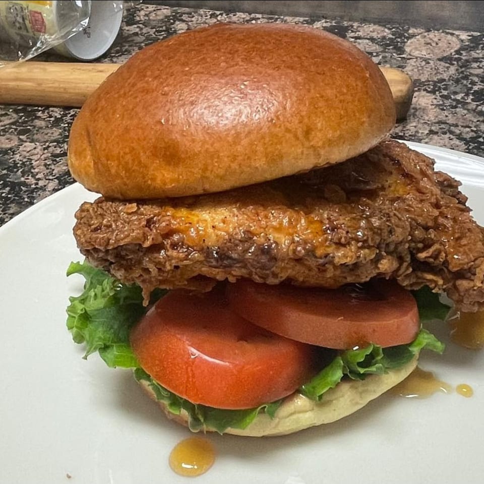 Courthouse Cafe's fried chicken sandwich with lettuce, tomato, and honey drizzle on a brioche bun.