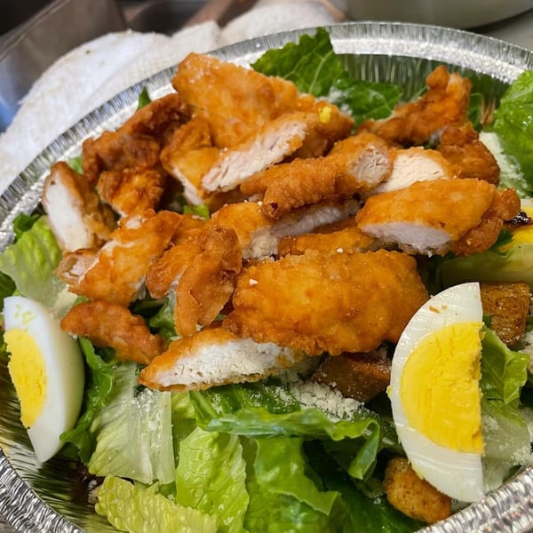 Crispy fried chicken pieces, hard-boiled egg, and croutons on a bed of fresh green lettuce.