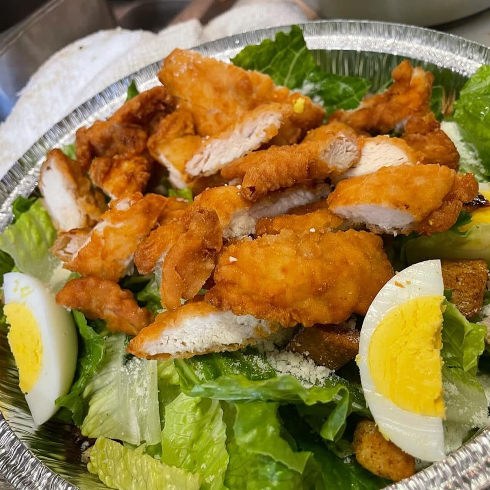 Crispy fried chicken pieces, hard-boiled egg, and croutons on a bed of fresh green lettuce.