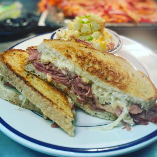 A grilled sandwich with meat and cheese, cut in half, served with a side of potato salad.