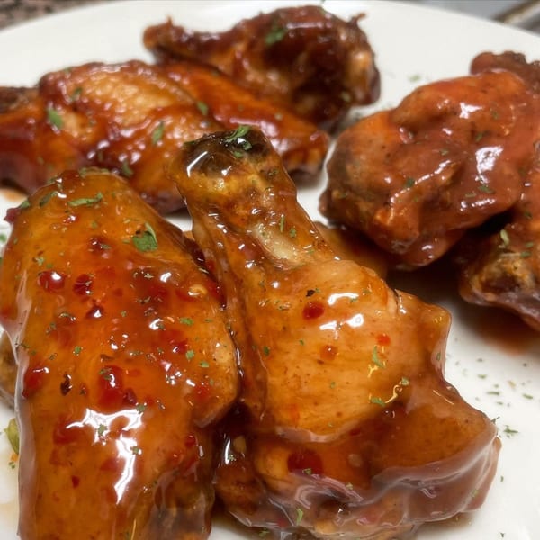 A close-up of several chicken wings coated in a glossy, reddish-brown sauce and sprinkled with herbs.